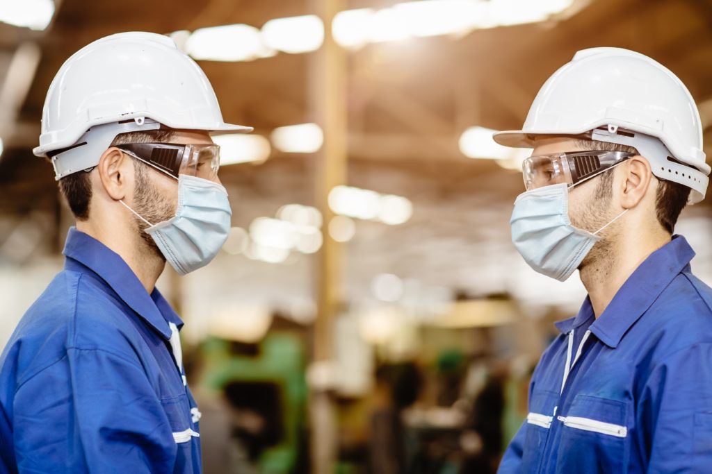 two employees wearing face masks and hardhats 